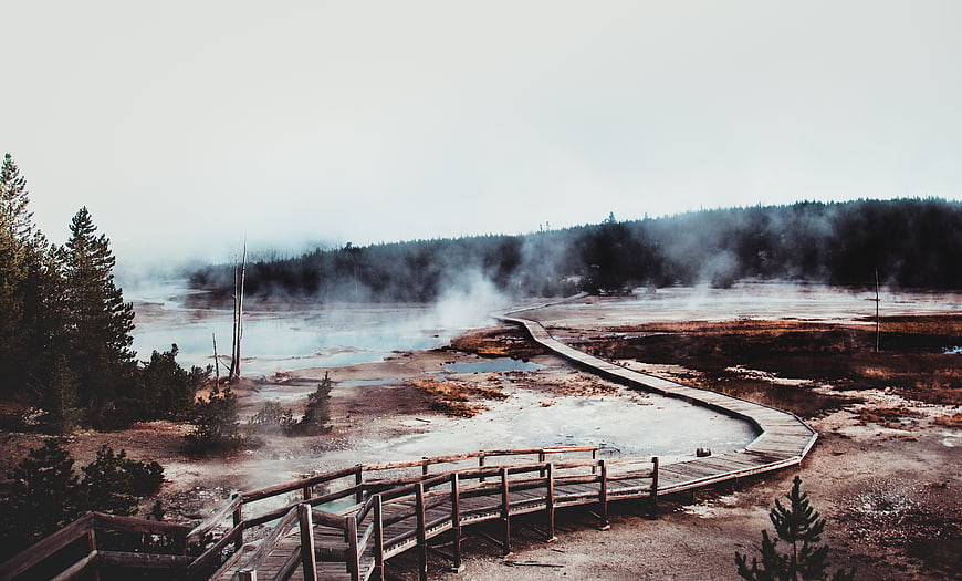 Misty wooden boardwalk winding through Yellowstone hot springs
