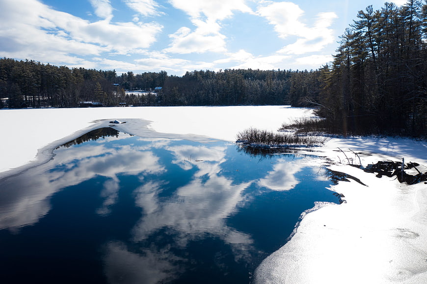 Frozen Lake with Blue Water Reflection in Winter Forest