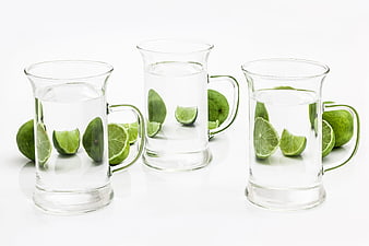 Three glass mugs with water and fresh lime slices on white background
