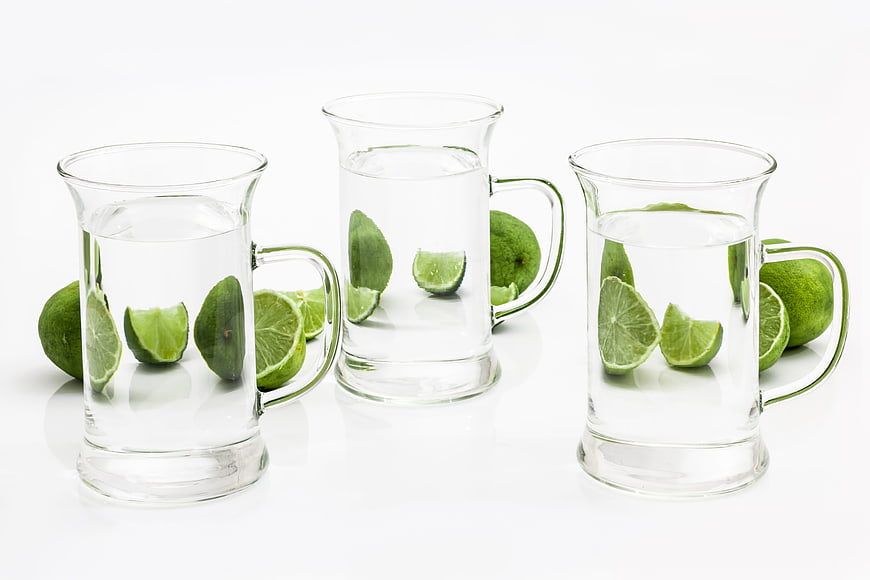 Three glass mugs with water and fresh lime slices on white background