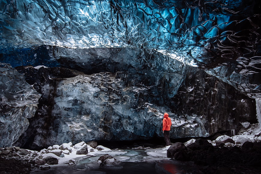 Person in Orange Jacket Exploring Blue Ice Cave