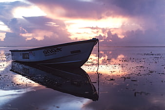Lone boat on calm water at sunset with purple clouds