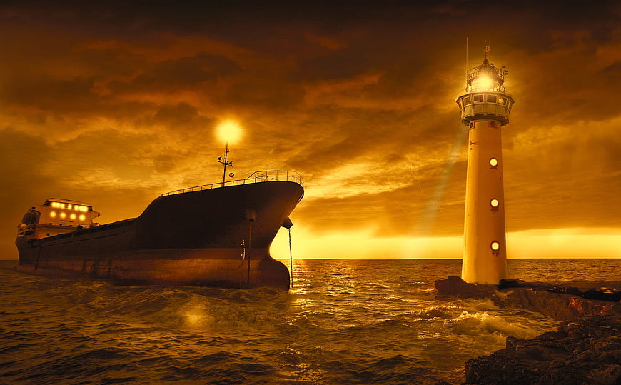 Cargo ship near lighthouse during dramatic golden sunset