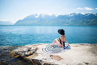 Woman in swimsuit relaxing on rocky shore with mountain lake view