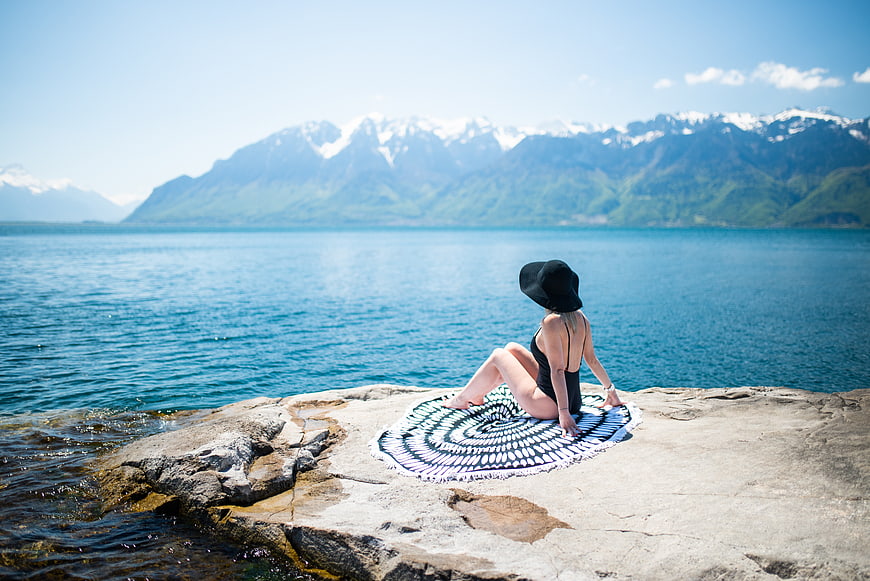 Woman in swimsuit relaxing on rocky shore with mountain lake view