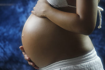 Close-up of pregnant woman holding belly against blue background