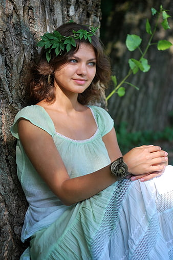 Young woman in green dress with leaf crown leaning against tree