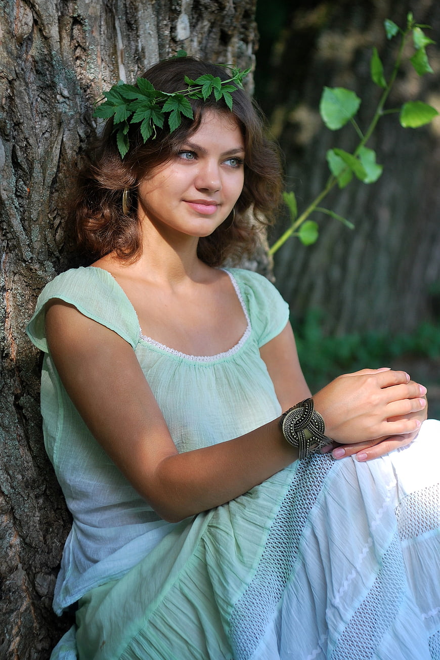 Young woman in green dress with leaf crown leaning against tree