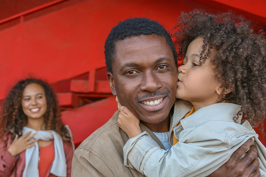 Happy Black Father Holding Daughter with Mother in Background