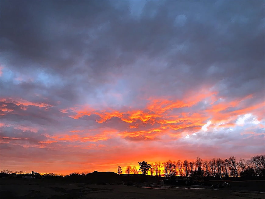 Dramatic fiery sunset over rural landscape with silhouetted trees