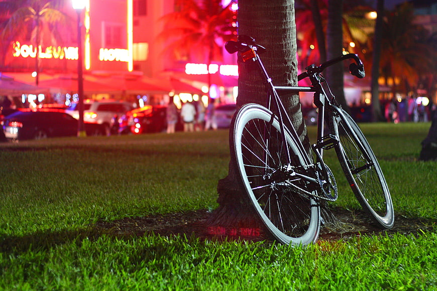 Black bicycle leaning against palm tree at night with neon lights
