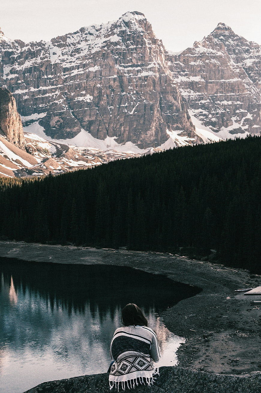 Woman wrapped in blanket sitting by mountain lake