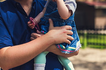 Father holding toddler child outdoors in denim overalls