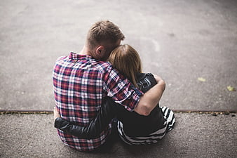 Couple sitting on pavement embracing from behind