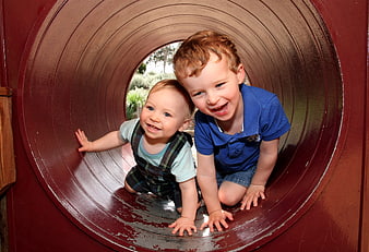 Two happy young boys playing inside a red playground tunnel