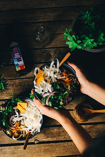 Top view of hands holding vegan noodle bowls on rustic wood