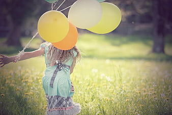 Child running in meadow holding colorful balloons