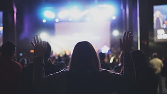 Silhouette of woman raising hands at concert stage
