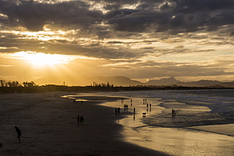 Dramatic Sunset Over Beach with Silhouetted People and Mountains