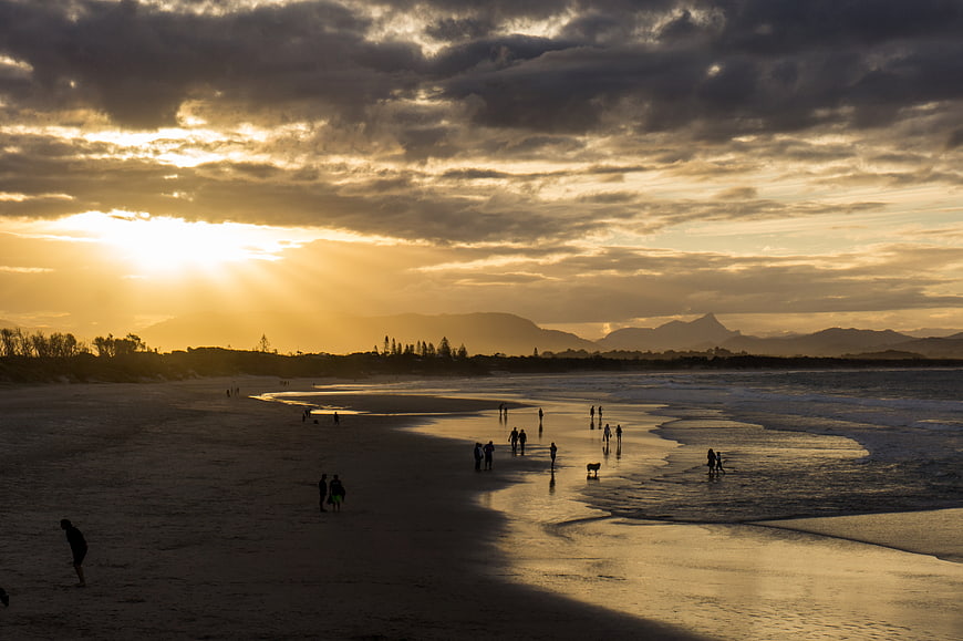Dramatic Sunset Over Beach with Silhouetted People and Mountains