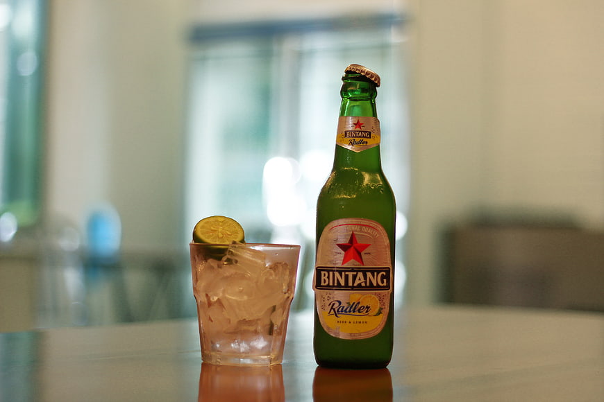 Bintang Radler beer bottle and iced drink with lime on table