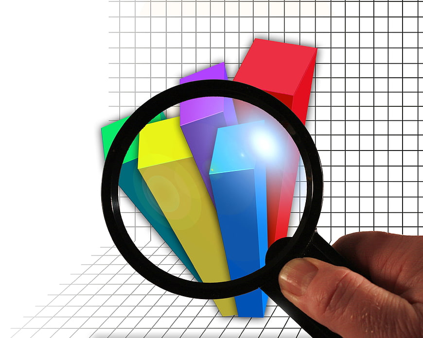 Hand holding magnifying glass over colorful 3D bar chart