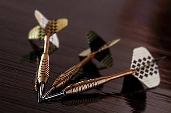 Three gold darts on dark wood surface
