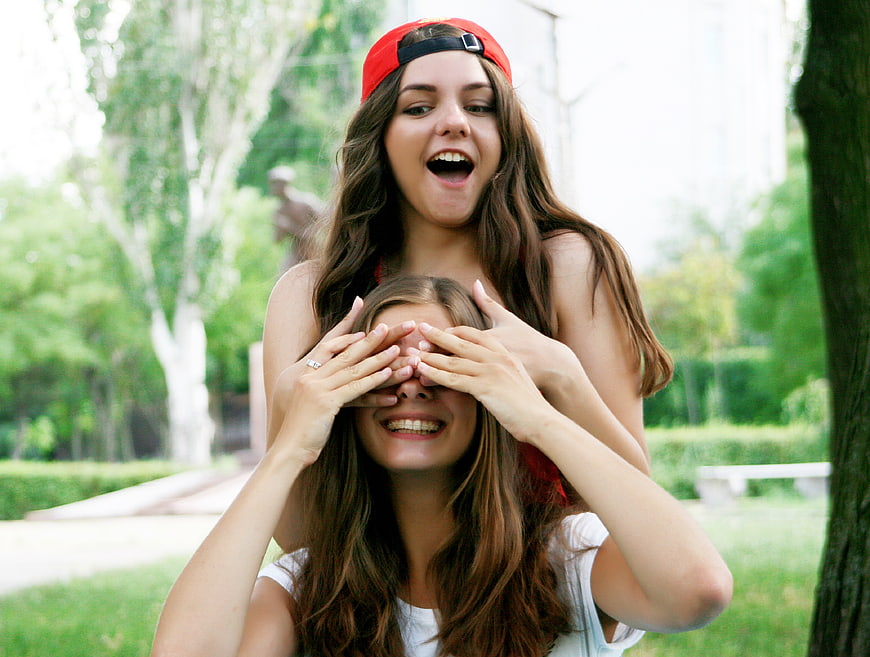Two happy young women playing peek-a-boo in a park