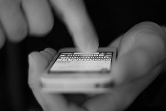 Close-up of hands typing on a smartphone keyboard in black and white