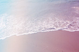 Pastel pink and blue ocean waves on sandy beach