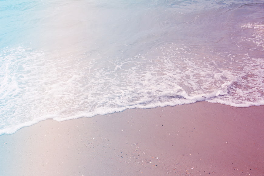 Pastel pink and blue ocean waves on sandy beach
