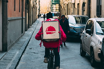 Food delivery cyclist riding down narrow European street
