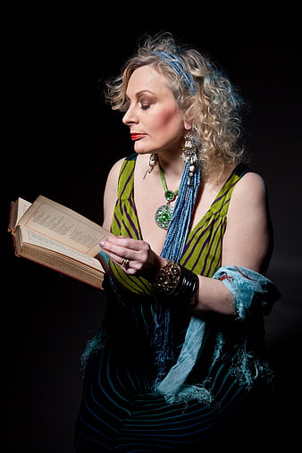 Mature woman with curly hair reading an open book in a dark studio