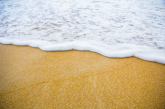 Close-up of gentle sea foam washing over golden sand