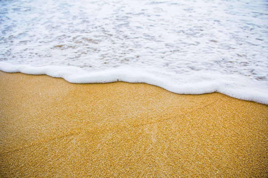 Close-up of gentle sea foam washing over golden sand