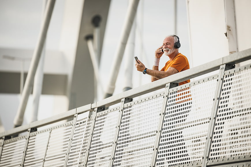 Senior man with headphones and smartphone on modern bridge