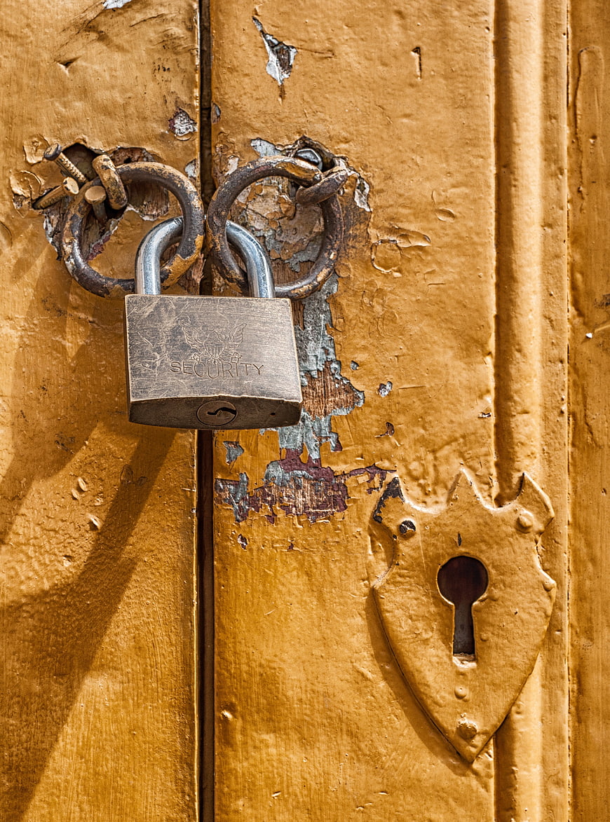 Close-up of silver padlock on weathered yellow wooden door