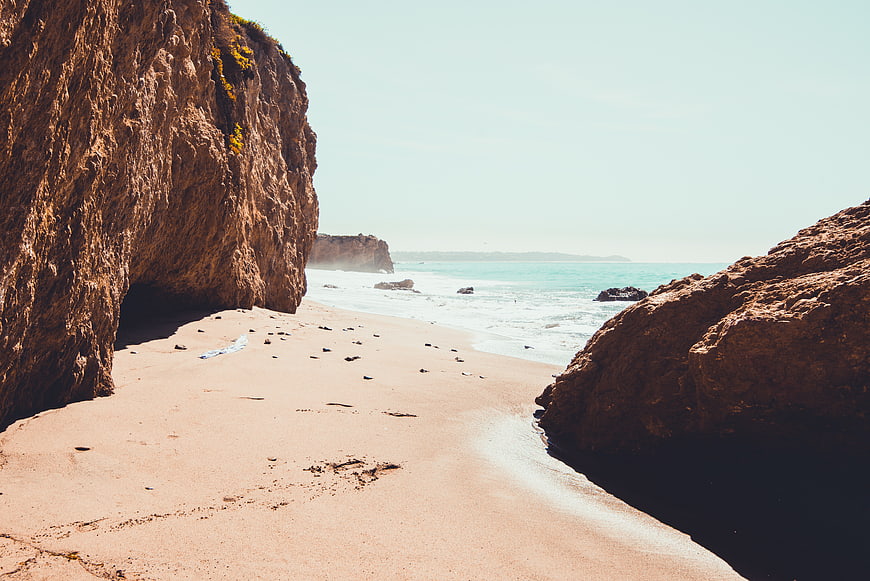 Sandy Beach Path Between Rocky Cliffs Leading to Ocean
