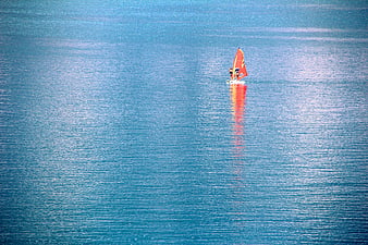Small sailboat with orange sail on calm blue lake