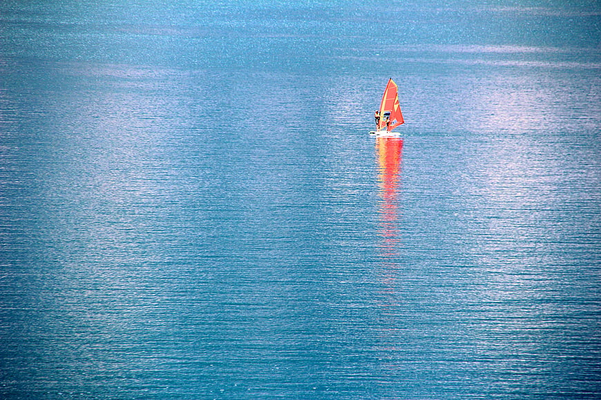Small sailboat with orange sail on calm blue lake