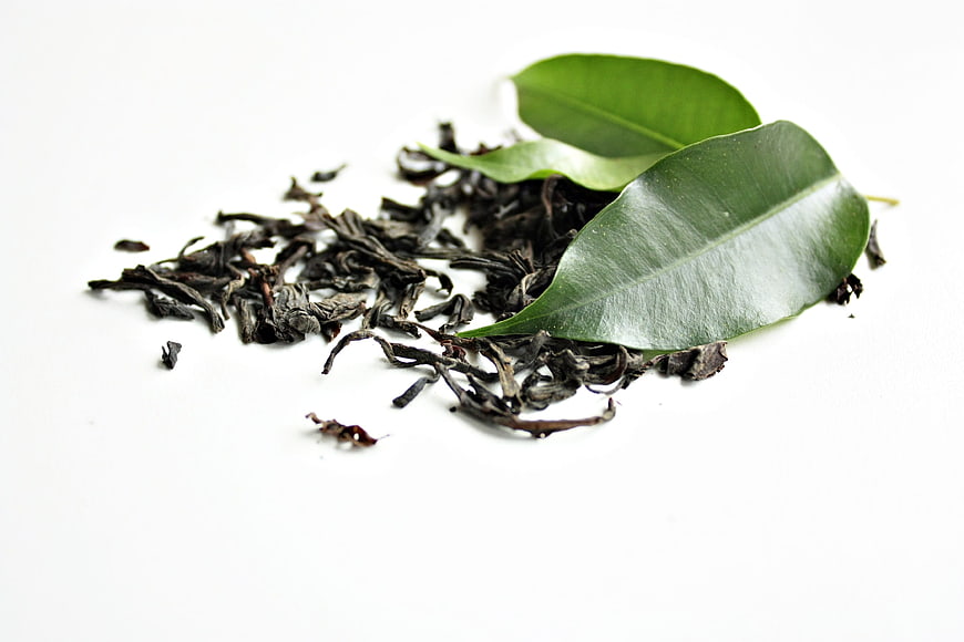 Dried Black Tea Leaves with Fresh Green Leaves on White Background