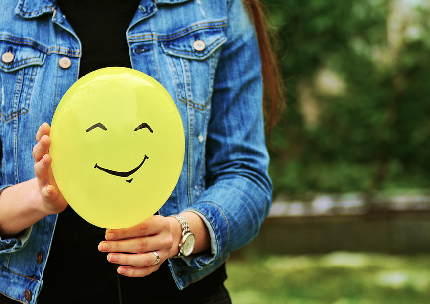 Woman holding yellow smiley face balloon outdoors