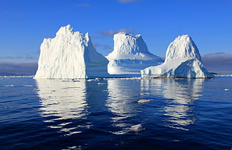 Three majestic icebergs floating in calm blue ocean water