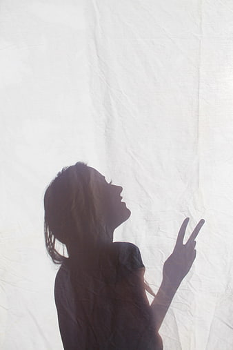 Silhouette of a woman making a peace sign behind a white sheet