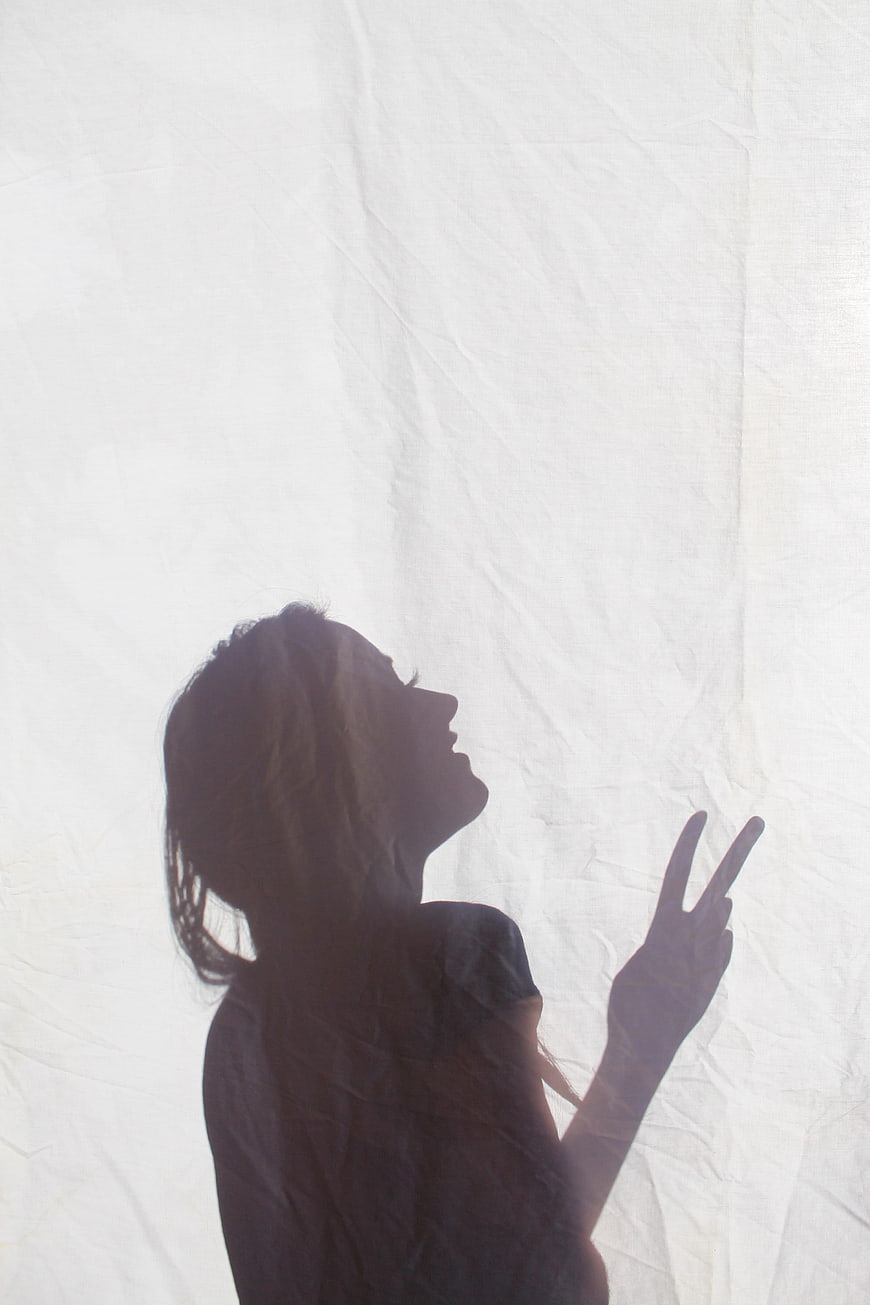 Silhouette of a woman making a peace sign behind a white sheet