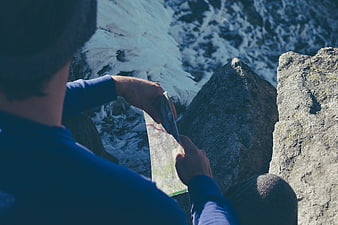 Hiker Checking Map on Snowy Mountain Cliff