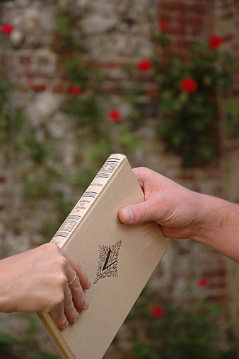 Hands exchanging a vintage book in a garden
