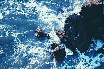 Aerial View of Turbulent Blue Ocean Waves Crashing Against Dark Rocks