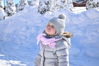 Happy child playing in snow wearing winter hat and scarf