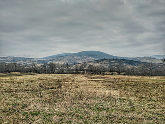 Overcast landscape with rolling hills and dry grass field